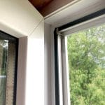 Close-up of Fliegengitter Fenster - mit Rahmen: white border, insect net in frame, trees visible outside.